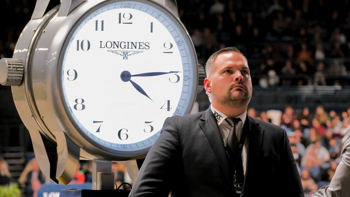 Sicherheitsmitarbeiter im Anzug bei einem internationalen Reitsportevent neben einer großen Longines-Uhr